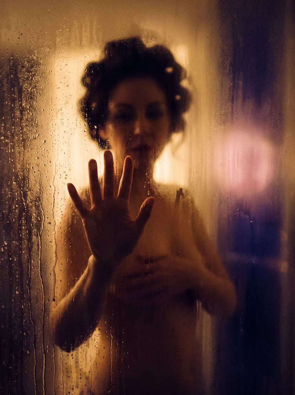 A woman behind fogged shower glass, her hand on the glass